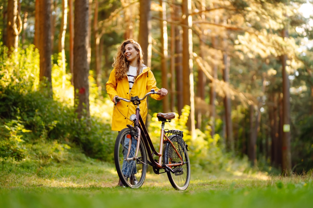 Young,Woman,In,Yellow,Coat,Riding,Bicycle,Park.,Active,Day.